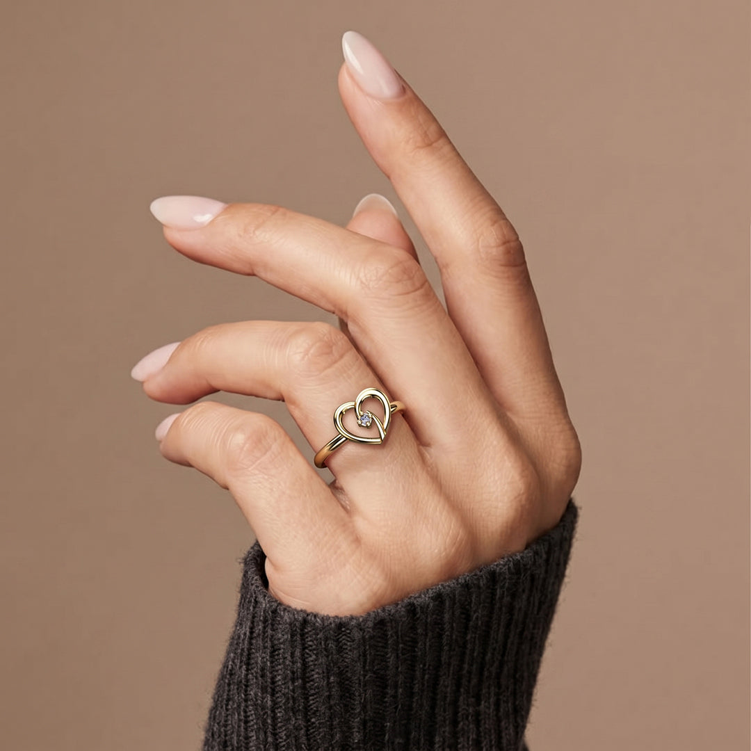 Golden heart solitaire ring worn on hand against a neutral background